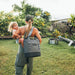 Woman carrying a child while wearing a YETI cooler bag in a backyard setting